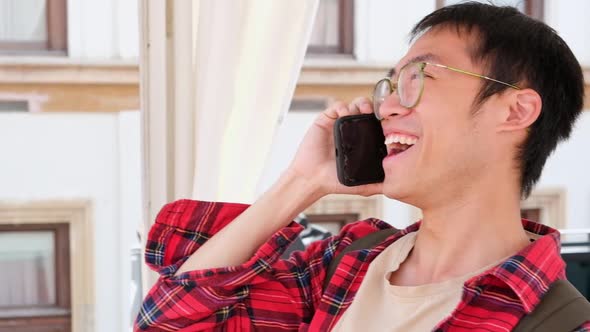 Asian Man Holding Smartphone and Talking By Phone with Friend Smiling and Laughing Outdoor