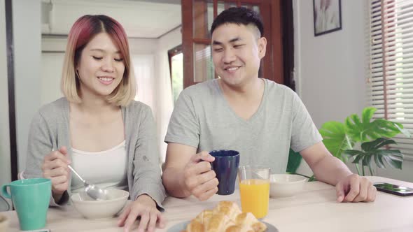 Happy sweet Asian couple having breakfast, cereal in milk, bread and drinking orange juice.