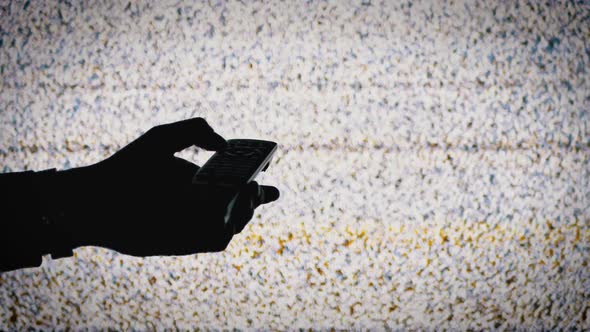 Silhouette of a Hand Holding a TV Remote on TV Screen Background with White Static Noise