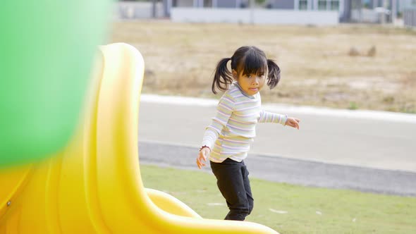 Joyful asian little girl playing on slider in playground