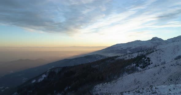 Side Aerial Top View Over Winter Snowy Mountain and Woods Forest at Sunset or Sunrise