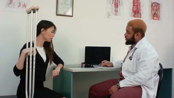 Female Patient with Crutches Discussing Her Condition with Doctor Making Notes