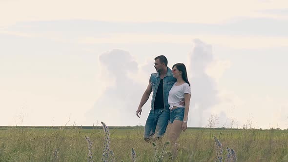 Couple Walks on Yellow Field with Flowers Under White Sky