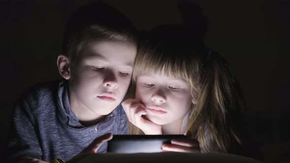 Two children brother and sister watching video on smartphone screen together. alt