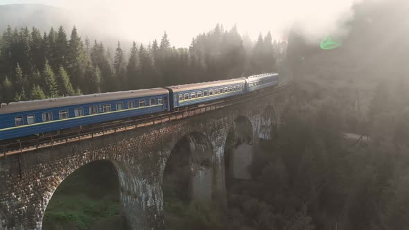 Aerial Shot of a Train Crossing a Beautiful Stone Bridge in Early Morning