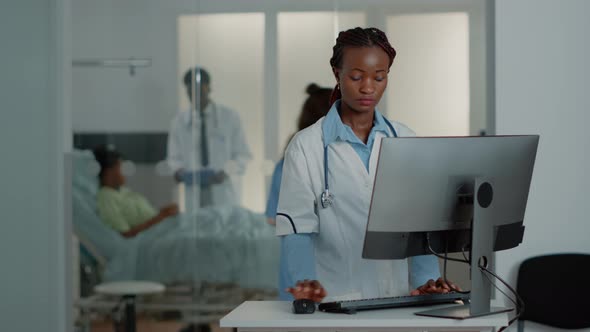 General Practitioner with White Coat Using Computer at Desk