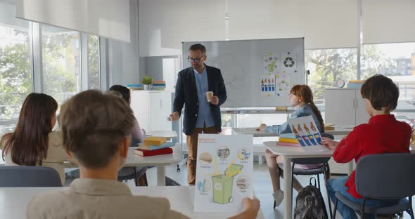 Back View of Diverse Teen Kids Sitting at Desk Having Ecology Lesson with Mature Teacher