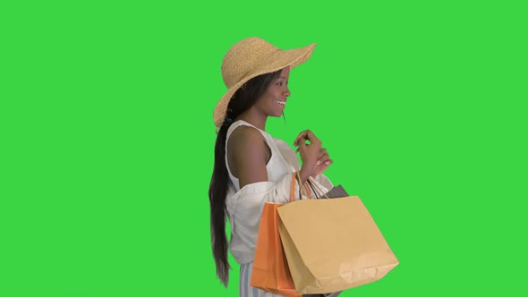 Smiling African American Woman in Straw Hat Posing with Shopping Bags on a Green Screen, Chroma Key