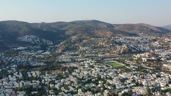 aerial view of Bodrum valley filled with white villas as the sun sets over the hills and homes in Mu