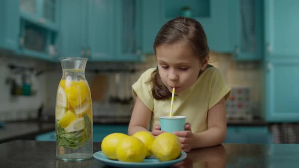 School girl in yellow dress drinking glass of homemade lemonade