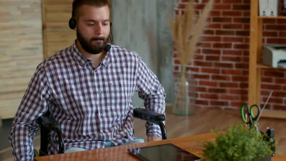 Bearded Caucasian Disabled Person Man in a Plaid Shirt and Jeans Wearing Work Headphone with