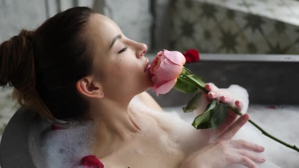 Sexy Girl Lies in a Big Stone Bath with a Rose Flower in Her Hands