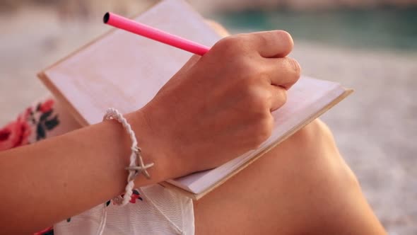 Close up view of a woman writing in her diary at sunset sitting on a beach