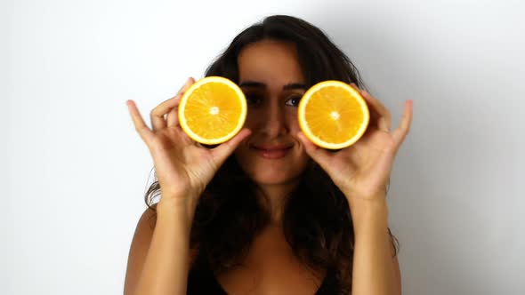 A beautiful mixed-race woman with dark hair smiling and dancing with oranges.