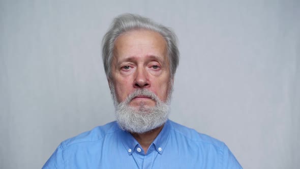 Closeup Portrait of Serious Grayhaired Mature Man Unemotionally Looking at Camera Standing on White