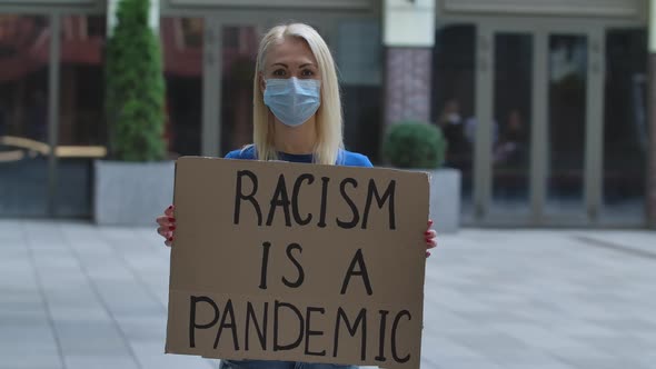 Outdoors Portrait of a Young White Female Activist Wearing a Medical Mask Holding a Cardboard Poster