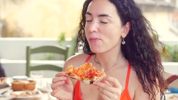 Young Cute Italian-looking Woman in a Red Dress Eagerly Eating and Enjoying Italian Pizza While in a