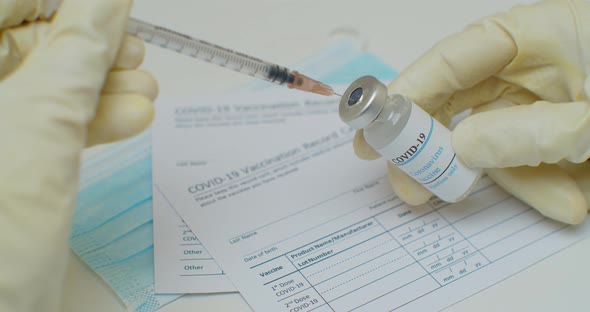 Close Up of Hand Filling a Syringe with Liquid From a Vial with a Label Reading Covid19 Vaccine