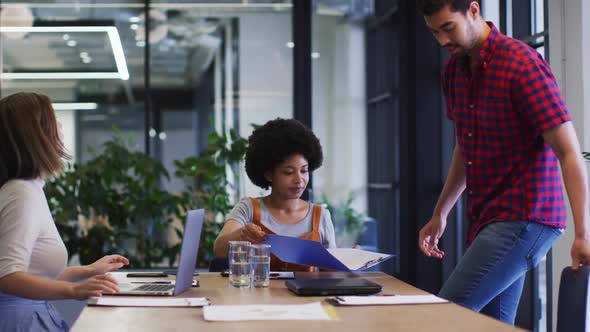 Diverse business people sitting using laptop going through paperwork in modern office