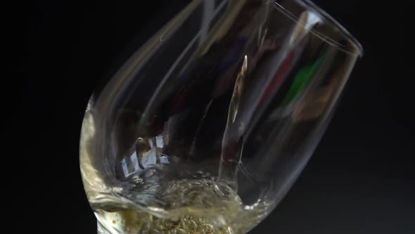 Wine is poured into a glass on a black background. Slow motion.