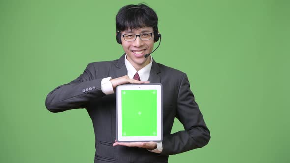 Young Asian Businessman Showing Digital Tablet To Camera While Working As Call Center Representative