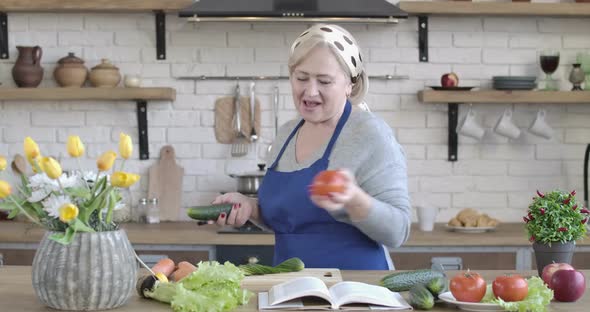 Nice Senior Caucasian Woman Smelling Fresh Vegetables and Starting Cooking Salad at Home