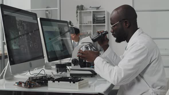 African American Engineer Examining Chip with Microscope