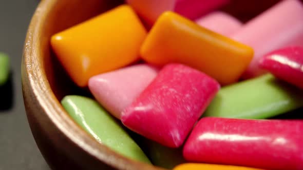 Multicolored chewing gum pads falling in slow motion into a wooden bowl. Colourful chew candy