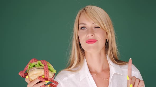 Woman Looking at Burger and Prohibits Junk Food on Green Background