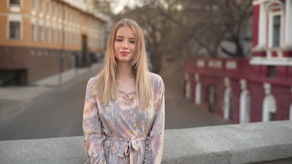 Portrait of Cute Blonde Woman 20s with Blond Hair Wearing Dress Smiling While Standing on Bridge in