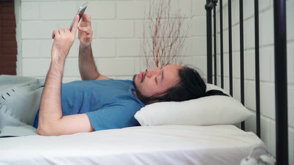 Asia male turn off alarm clock in mobile phone after awake on bed in bedroom at home.