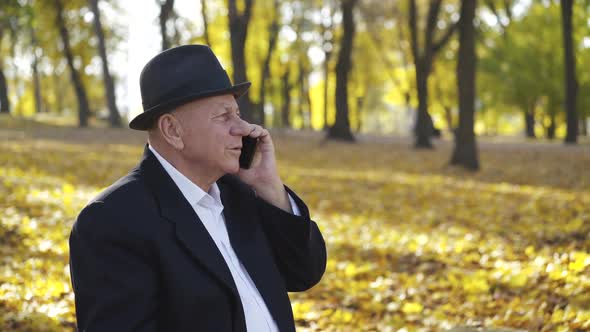 Handsome Senior Man in Hat Takes the Call and Has Fun Talks on the Mobile Phone