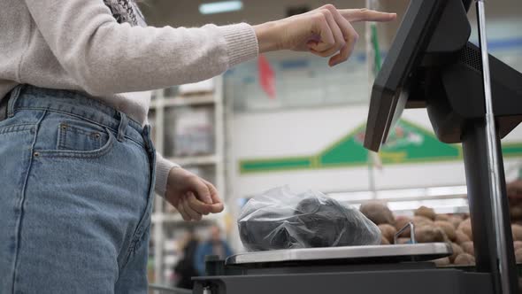 Young Woman Weighs Avocados in Plastic Bag in Supermarket