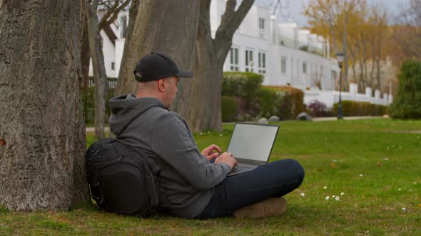 Young Man is Sitting in a Park in a Tourist Place Working on a Laptop