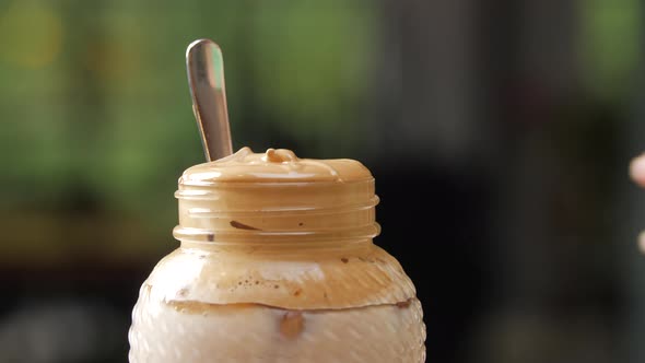 Female Hand Picking Up a Homemade Dalgona Coffee in a Mason Jar