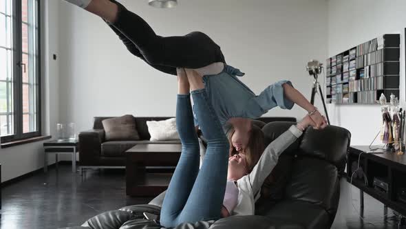 Teenage girl balancing friend on her feet lying on sofa