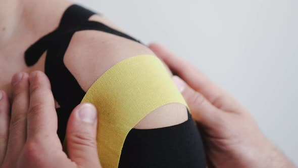 Closeup of Process of Placing Kinesiology Tape on Man's Shoulder