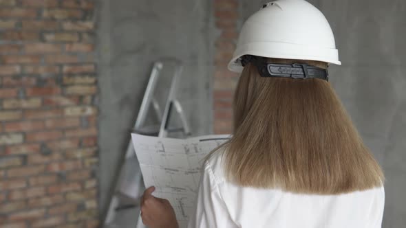 The girl engineer builder is checking the drawings at the apartment of the projected house.