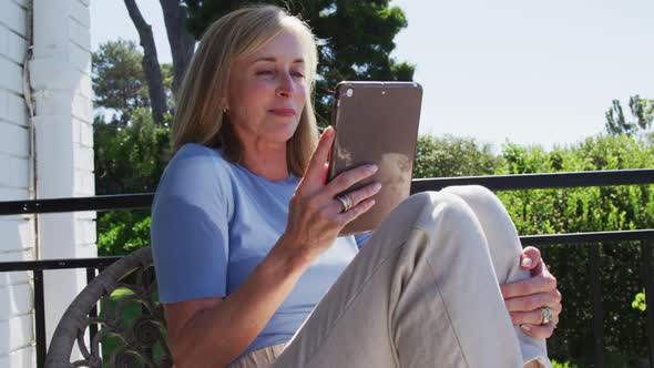 Senior caucasian woman using tablet sitting in sunny garden