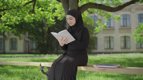 Portrait of Confident Muslim Woman Enjoying Reading Outdoors on Sunny Day. Happy Young University