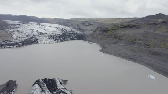 Aerial view over the Solheimajokull glacier lagoon, in cloudy Iceland - reverse, drone shot