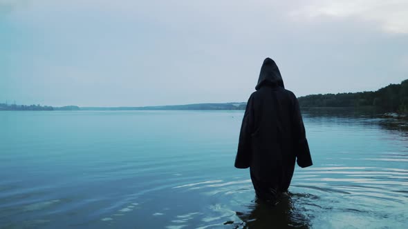 Female figure in a black robe enters the water. Halloween costume