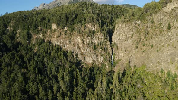 Aerial lowering on a pine tree woodland with Corbata Blanca waterfall between steep mountains, Patag