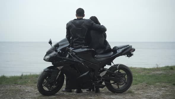 Wide Shot of Black Motorcycle with Loving Couple Hugging at the Background. Happy Interracial