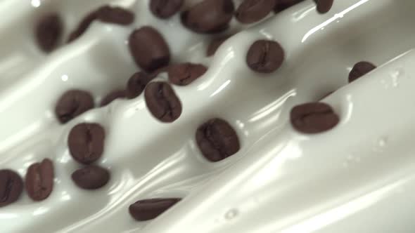 Flying coffee beans mix into flowing milk in slow motion. Close up