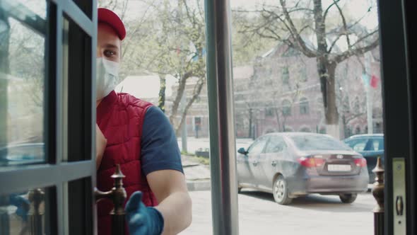 Postman or Delivery Man in Mask During Coronavirus Carry Small Box Food Deliver to Young Woman