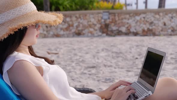 Panning close up shot of a carefree Asian woman using laptop computer at beach