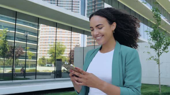 Happy Pretty Brazilian or Hispanic Young Woman with Curly Hair Stylishly Dressed Using Her