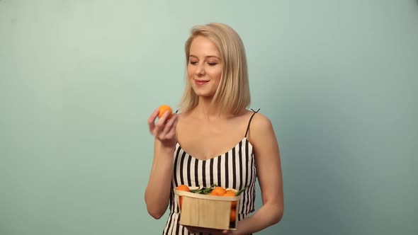 Smiling woman with orange in dress on blue background