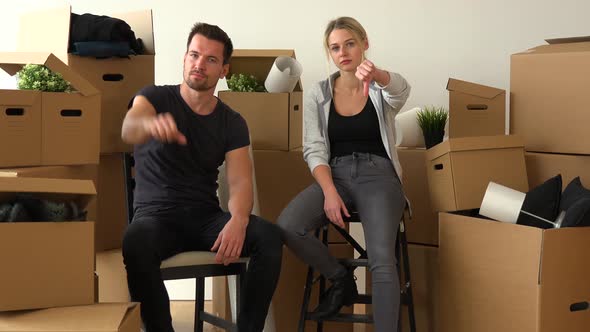 A Unhappy Moving Couple Sits on Chairs, Shakes Their Heads and Shows a Thumb Down To the Camera